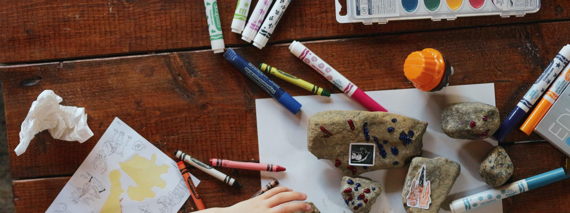 Bastelmaterialien und Stifte mit denen ein Kind am Tisch spielt