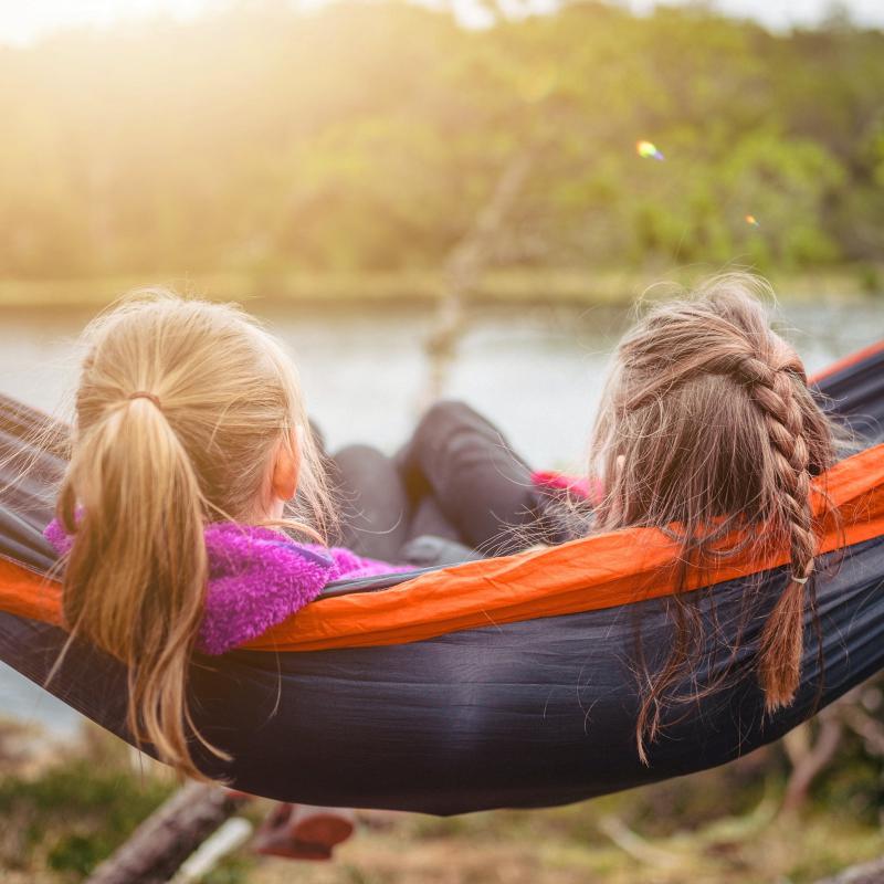 Zwei Kinder sitzen in Hängematte und schauen auf See